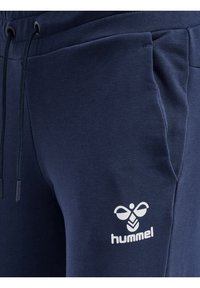 Marinblå sweatpants gjorda av mjukt tyg, med sidofickor och dragsko i midjan, med en vit logotyp på nederbenet.