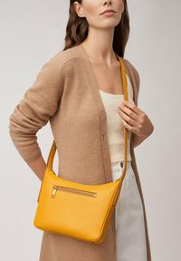 Sacoche en cuir jaune avec une texture lisse, dotée d'une poche avant zippée et d'une sangle ajustable fine.