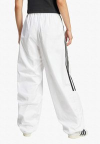 White, loose-fitting tracksuit pants with an elastic waistband, featuring black side stripes and cuffs; made of lightweight material.