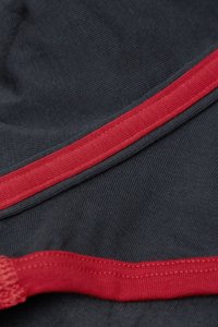 Tmavá tkanina s ribbed texturou, s výrazným červeným akcentem po okraji. Hladký povrch, dobře ušité švy.