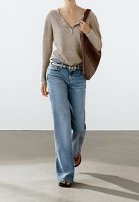 Beige ribbed sweater with a buttoned neckline, light blue wide-leg jeans, and a woven brown tote bag. Black sandals with red accents.