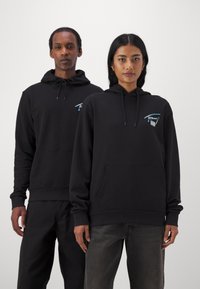 Sudaderas negras hechas de una tela suave, con un bolsillo frontal y capucha con cordón. Cada una tiene un pequeño logo turquesa en el pecho.
