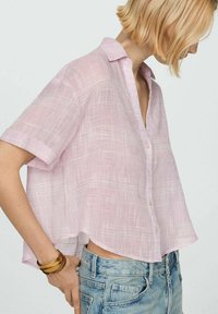 Camicia di lino rosa chiaro con maniche corte, bottone frontale, vestibilità rilassata e una sottile trama. Abbinata a pantaloni shorts in denim blu chiaro.