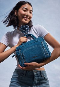 Borsa in denim blu con due cerniere laterali, manici superiori e dettagli con logo. Il design presenta una forma strutturata e un tessuto testurizzato.