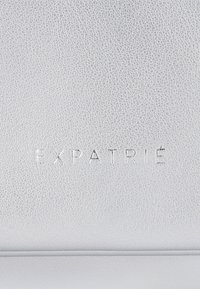 Szara skórzana tekstura z wytłoczonym logo "EXPATRIÉ", prezentująca gładką powierzchnię z delikatnymi wzorami ziarna i minimalistycznym wzornictwem.