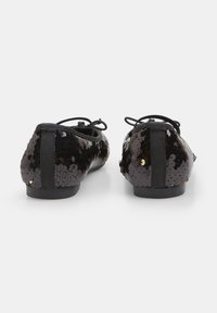 Black flat shoes covered with sequins, featuring a rounded toe, elastic accents on the sides, and smooth black soles.