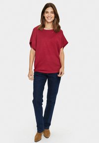 Haut rouge à manches courtes avec une coupe décontractée. Associé à un jean droit bleu foncé et des bottes de cheville en suède marron. Design simple et décontracté.