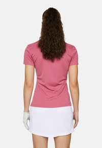 Roze shirt met korte mouwen, voorzien van een getailleerd ontwerp, een gladde textuur en een ronde hals. Gecombineerd met een witte rok, wat een sportieve uitstraling creëert.