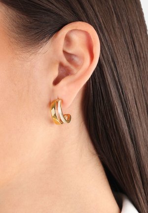 Los pendientes en tono dorado presentan un diseño curvado y superpuesto con superficies lisas y texturizadas, mostrando acabados brillantes y mate.