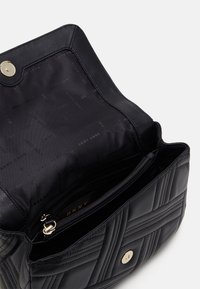 Czarna pikowana torebka z złotymi okuciami. Wnętrze wyposażone w kieszeń na zamek i logo DKNY, podkreślające jej strukturę i gładką fakturę.