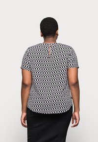Black and white patterned short-sleeve top with a round neckline and keyhole back detail. Smooth texture, slightly curved hemline.