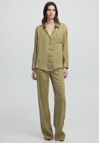 Camisa de botón de manga larga en verde oliva con un bolsillo en el pecho, combinada con pantalones de pierna ancha a juego, ambos en una tela suave.