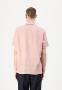 Camicia rosa a maniche corte realizzata in tessuto leggero. Presenta un colletto, maniche arrotolate e una vestibilità rilassata. Texture sottile visibile.
