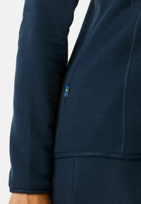 Marineblauwe fleece jack met een gestructureerd oppervlak, een halve rits en een klein accent van de Zweedse vlag nabij de zoom. Zacht en warm materiaal.