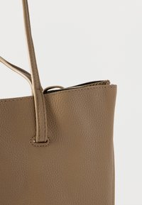 Μπεζ δερμάτινη τσάντα tote με υφή στην επιφάνεια, δύο λουριά για τον ώμο και άνοιγμα στην κορυφή, με εμφανείς ραφές και καλοσχηματισμένο σχήμα.