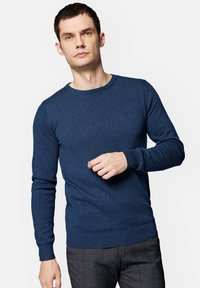 Granatowy sweter z okrągłym dekoltem, wykonany z miękkiego materiału, z długimi rękawami oraz ściągaczami przy mankietach i u dołu. Mały detal logo na piersi.