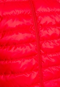Veste rembourrée rouge avec une texture lisse et brillante, dotée de sections matelassées horizontales et d'un zip central.