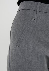Pantalons gris ajustés offrant une texture lisse, une coupe droite et une poche latérale épurée avec un détail de couture subtil.
