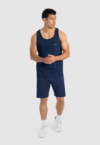 Camiseta sin mangas y pantalones cortos atléticos de color azul marino, confeccionados con tela ligera. Presentan un cuello redondo y un detalle de logotipo en la camiseta.