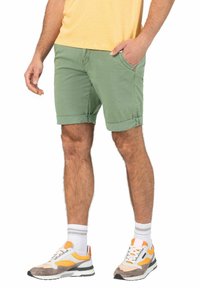 Hellgrüne Shorts mit umgeschlagenen Säumen, Seitentaschen und einem kleinen roten Logo; kombiniert mit grauen Sneakers mit orangefarbenen Akzenten und weißen Socken.