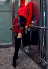 Červený rolák s pleteným vzorem, károvaná minisukně v červené, modré a žluté, černé ponožky nad kolena a černá kabelka. Pozadí výtahu.