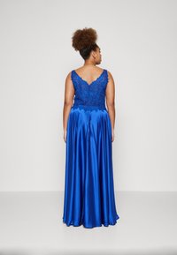 Kuningan malam biru royal dengan bodice renda, punggung v, dan rok satin yang mengalir. Memiliki detail renda yang halus dan tekstur yang lembut.