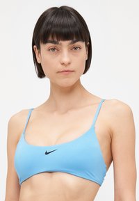 Svetlomodrý bikini vrch s tenkými popruhmi, vyrobený z hladkej látky. Na prednej strane sa nachádza čierne logo Nike swoosh.