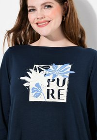 Marinblus med långa ärmar som har ett blommönster och ordet "PURE" i fet svart text. Mjuk tyg med avslappnad passform och vid halsringning.
