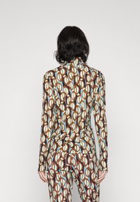 Langemouwen top en bijpassende broek van rekbare stof, met een abstract patroon in bruin, crème en turquoise.