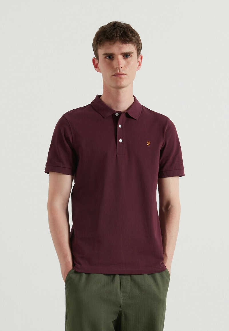 Burgundowa koszulka polo wykonana z bawełny, z zapięciem na guziki przy kołnierzyku oraz małym żółtym logo na piersi. Krótkie rękawy i prosty krój.