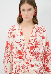 Witte bloemen blouse met rood botanisch patroon, V-hals en gathered detail bij de taille. Vloeiende stof met vleermuismouwen.