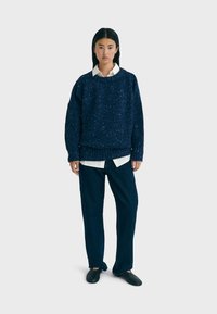 Pull en maille texturée marine à col rond, superposé à une chemise blanche à col. Associé à un jean sombre ample et des chaussures noires.