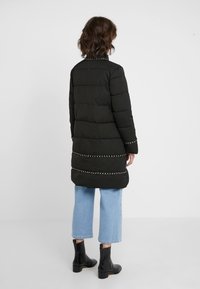 Długa czarna kurtka puchowa z poziomym przeszyciem i ozdobnym łańcuszkiem na dole. Noszona z jasnoniebieskimi, skróconymi jeansami i czarnymi botkami.