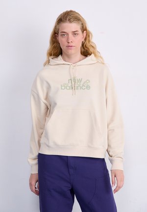 Beige huppari, jossa on etutasku ja nyöripään, sisältäen vihreän graafisen "new balance" -logon. Yhdistetty purppurapantoihin.