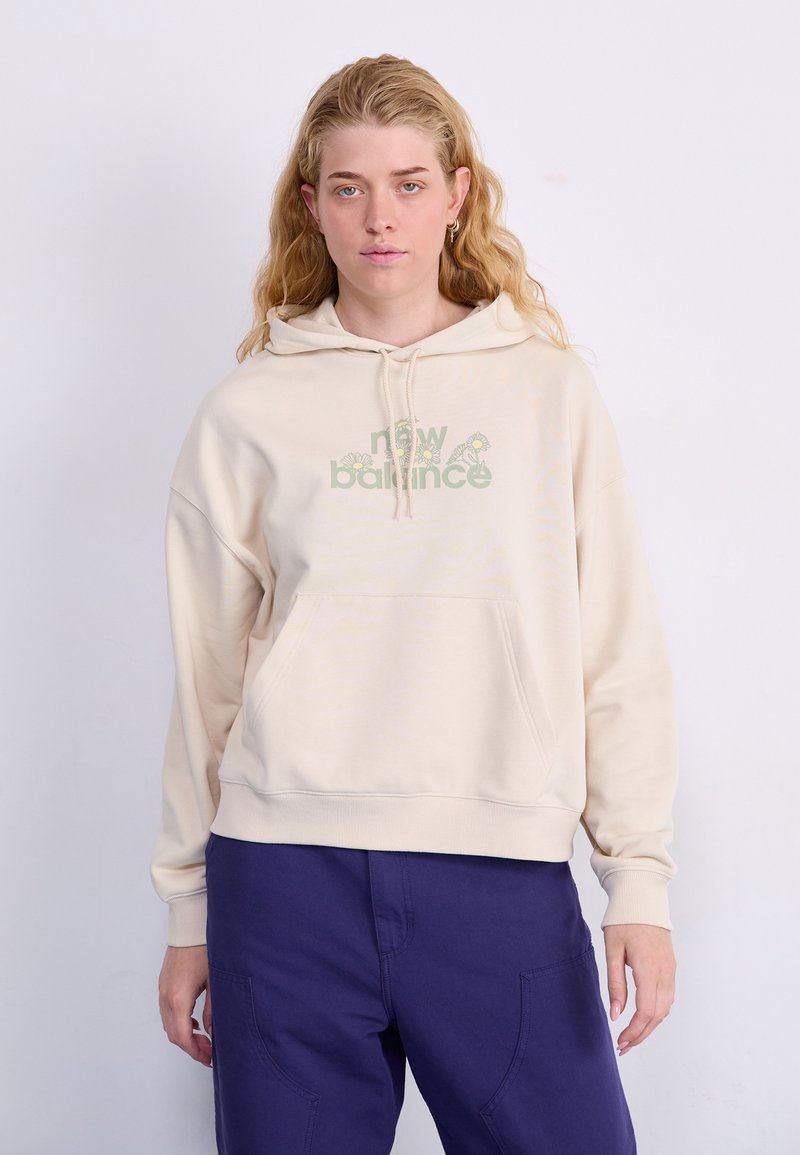 Beige hettegenser med frontlomme og justerbar hette, med en grønn grafikk "new balance" logo. Brukt med lilla bukser.