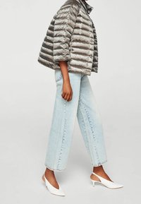 Pöyhkeä hopeinen toppatakki pystykorkealla kauluksella, vaaleansiniset leveälahkeiset farkut ja valkoiset slingback-korkokengät, jotka esittelevät sileitä pintoja ja modernin siluetin.