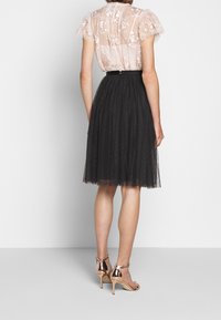 Haut transparent blush avec broderies florales, jupe en tulle noir et talons métalliques à lanières. La jupe présente une taille froncée et un motif à pois.