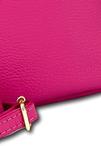 Roze synthetisch materiaal met een gestructureerde afwerking, voorzien van een gouden hardwaredetail op een band. Het ontwerp is slank en minimalistisch.