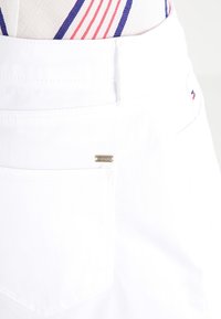 Witte denim rok met een achterzak voorzien van een klein gouden logo plaatje. Subtiele stiksels benadrukken het schone, minimalistische ontwerp.