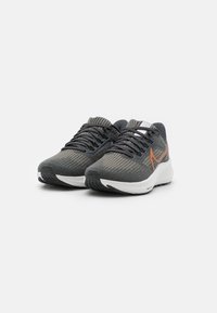 Een paar zwart-grijze hardloopschoenen met een oranje logo en een witte zool, geplaatst op een witte achtergrond.