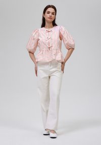 Gestreiftes Peplum-Top in Rosa und Weiß, mit Puffärmeln und Vorderbindung. Kombiniert mit weißen Schlaghosen und Schuhen mit schwarzen Akzenten.