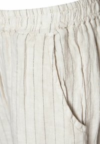 Ľanové nohavice v svetlej béžovej farbe s čiernymi vertikálnymi pruhmi. Majú elastický pás a bočné vrecká. Mäkká textúra zvyšuje pohodlie.