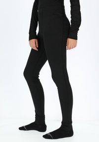 Sort ribbestrikkede leggings lavet af strækbart materiale, der har et højt talje design og glat tekstur, parret med sorte ankelstrømper.