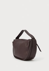 Temno rjava teksturirana usnjena torba za ramo s širokim nastavljivim trakom in zadrgo, postavljena poševno na enobarvnem svetlem ozadju.