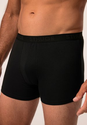 Boxer-briefs noirs en tissu doux avec une taille élastique présentant un logo en relief "STHUGE". Texture lisse et design ajusté.