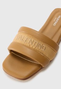 Sandale à enfiler tan avec une large sangle en tissu arborant le logo "Valentino", tige en cuir lisse, semelle plate et design de bout arrondi.