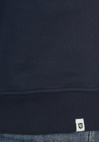 Navyblauwe sweatshirt met een geribde zoom, voorzien van gestikt detail en een klein wit merklabel in de linksonderhoek.