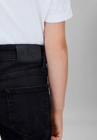 Vaqueros de mezclilla negra con una textura suave, que presentan un parche con el logo de Calvin Klein en la cintura trasera y un bolsillo trasero.