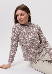 Top met lange mouwen in beige met een bordeauxrode geometrische print, voorzien van een hoge halslijn en een losse pasvorm, gecombineerd met lichtgekleurde broek.