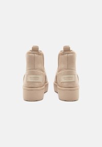 Bottes de cheville beiges en daim souple, avec un col rembourré, une languette et une semelle en caoutchouc à finition texturée. Étiquette avec logo à l'arrière.